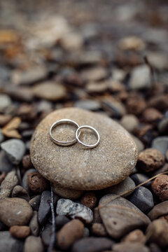 Three wedding rings placed on a smooth stone surrounded by natural pebbles, symbolizing unity, love, and connection.
Three Wedding Rings on Stone Among Pebbles