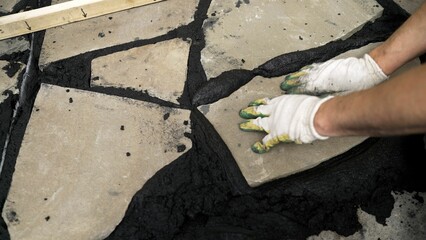 Construction worker carefully placing irregular shaped stone on wet mortar during a paving project