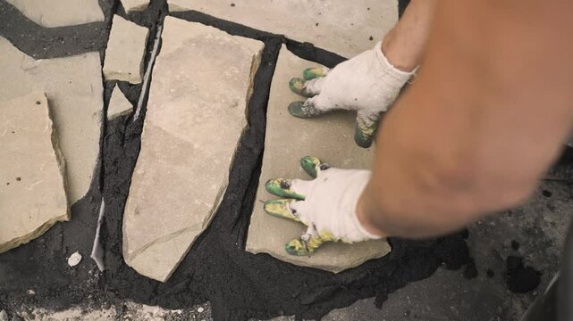 Construction worker carefully placing irregular shaped stone on wet mortar during a paving project