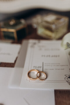 Close-up of two wedding rings placed on elegant invitation cards with greenery design, surrounded by soft wedding details. Wedding Rings on Invitation Cards with Floral Details 
