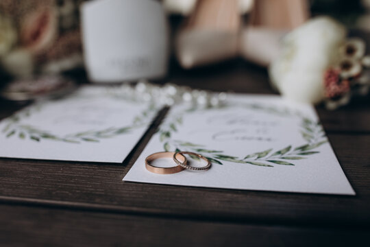 Close-up of two wedding rings placed on elegant invitation cards with greenery design, surrounded by soft wedding details. Wedding Rings on Invitation Cards with Floral Details 