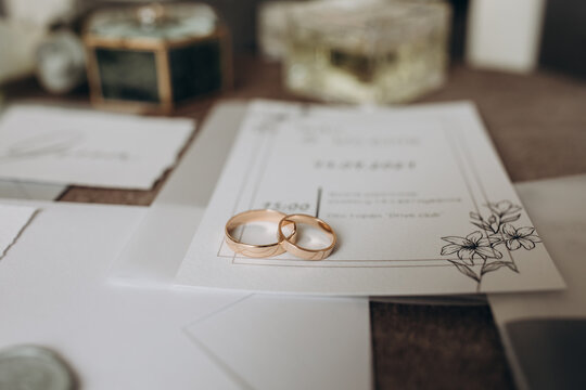Close-up of two wedding rings placed on elegant invitation cards with greenery design, surrounded by soft wedding details. Wedding Rings on Invitation Cards with Floral Details 