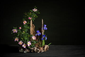 A serene ikebana arrangement featuring a delicate branch of wild rose and elegant irises. The naturalistic composition exudes harmony, simplicity, and quiet beauty