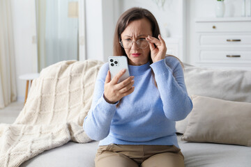 Woman with vision problem using smartphone on sofa at home