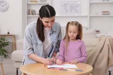Mother teaching her daughter to draw at table indoors