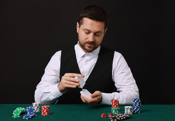 Professional croupier shuffling cards at gambling table against black background