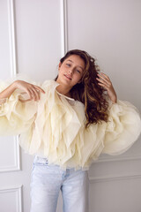A portrait of a fashionable teenage girl in blouse and sneakers dancing in a studio on a light wall in a room. light from the window