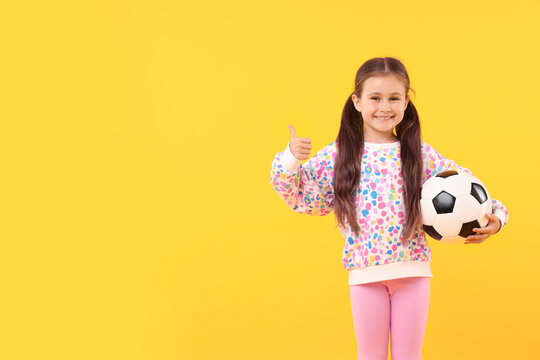 Little girl with soccer ball showing thumbs up on yellow background, space for text