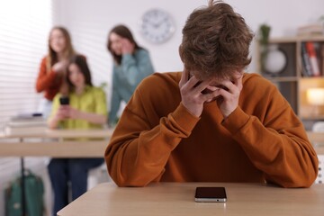 Teenage boy with smartphone suffering from bullying at school, selective focus