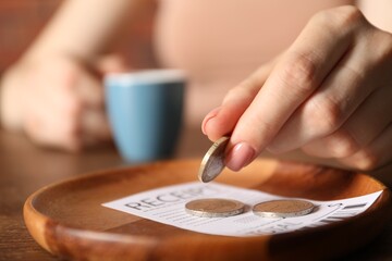 Woman putting tips onto plate at table in cafe, closeup