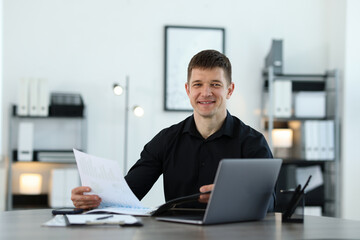 Handsome man working with documents at desk in office. Space for text