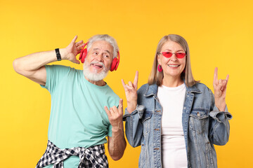 Senior couple in stylish outfits making rock gestures on orange background