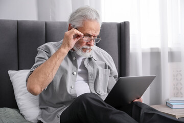 Senior man with vision problem using laptop on bed at home