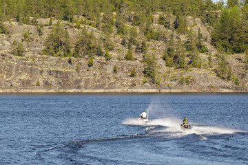 Two people ride jet skis across a peaceful lake surrounded by forested cliffs, capturing the thrill...