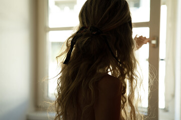 Silhouette of Woman with Long Hair Opening Window in Soft Morning Light
