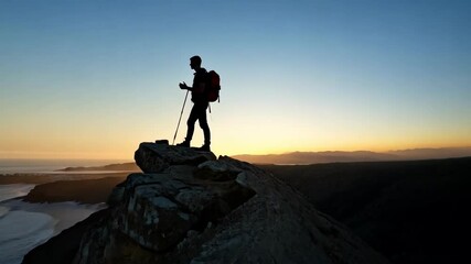 Silhouette of hiker on a cliff overlooking the ocean at sunrise - Powered by Adobe