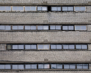 Old gray brick industrial facade featuring repetitive horizontal windows, some damaged or open,...