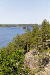 Rocky pine-covered cliffs overlook a calm blue lake with small wooded islands, surrounded by dense...