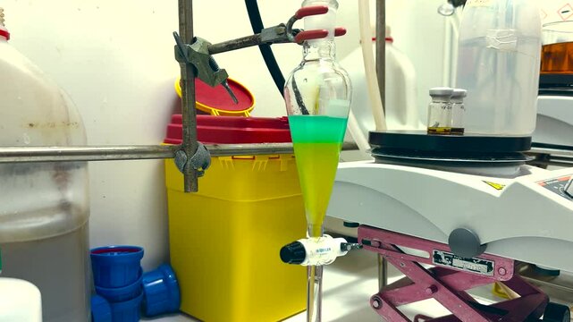 Separation of organic layer and water layer in separating funnel in a chemistry lab for education purpose. Effervescent of carbon dioxide bubble in organic layer. 4K scientific background concept.