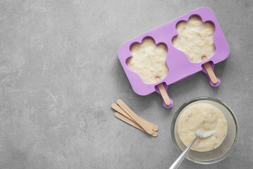 Silicone mold in paw shape, creamy mixture in a bowl, and wooden sticks for homemade banana ice...
