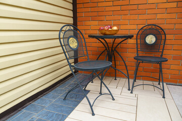 Small metal table with  bowl of fruit is flanked by two metal chairs against brick wall