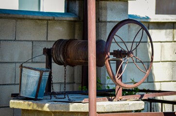 A rusty old water pump is hanging from a chain. The chain is attached to a bucket. The bucket is...
