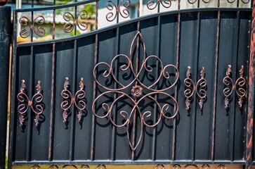 A wrought iron gate with a flower design on it. The gate is black and has a gold trim