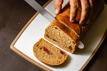 Horizontal photo of a brown adult man's hands slicing whole wheat bread with guava jam on a cutting...