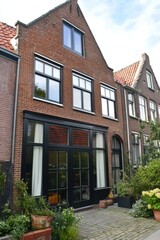 This delightful brick house features expansive windows that invite natural light and a lovely garden, all situated in a scenic neighborhood on a bright, sunny day