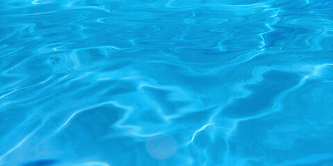 Abstract background of clear blue water with sun reflections in a swimming pool