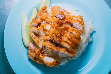 Crispy Chicken Fillet Served on a Bed of Rice with Fresh Cucumber Slices on a Light Blue Plate
