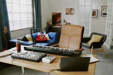Modern home studio showing digital piano, DJ controller, audio mixer, microphone, laptop on desk...