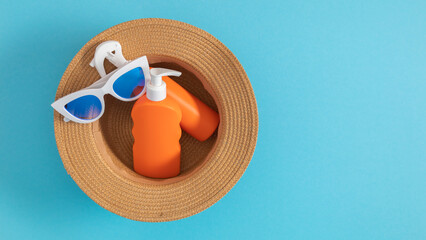 Top view of straw hat, glasses and orange sunscreen, lotion and cream, on blue background. Safe tanning concept on the beach