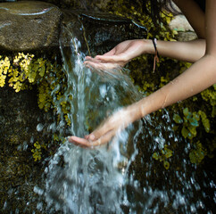 A close-up image of a person's cupped hands collecting water from a small natural stone ledge...