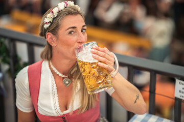 Traditional dirndlwearing woman drinks a full liter of beer at a Bavarian folk festival in a large...