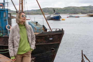 Woman standing near rusty abandoned fishing boats at the ship graveyard in Teriberka