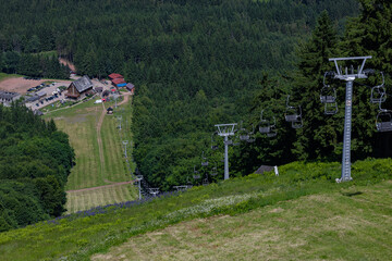 Mountain resort with hiking trails and empty chairlift among green forested slopes and alpine...