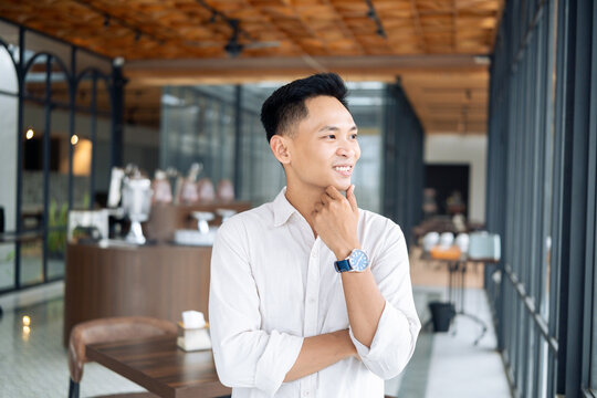 A young man dressed in business casual attire poses confidently in a stylish coffee shop with contemporary decor, conveying a professionalism and a vibrant entrepreneur spirit.
