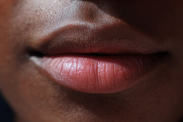 Obraz premium Close-up of lips with natural texture and deep brown skin tone showing subtle light reflections and smooth softness, highlighting skin detail and healthy appearance.