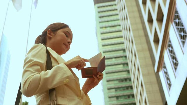 Asian female tourist checks passport validity in front of city office building and checks air ticket in preparation for travel.