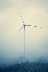 Wind turbine stands tall amidst foggy Alpine mountains, showcasing renewable energy in a serene...