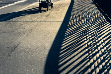 Shadows cast by a stroller on a sunny street with mountains in the background at dusk in the Alps