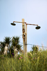 Rusty pole supporting two old lamps amidst tall grass in the Alps under a clear sky