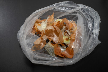 Onion peel in bio bag on black table and vegetable peeler.Close up of dry onion peel as...