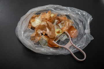 Onion peel in bio bag on black table and vegetable peeler.Close up of dry onion peel as...