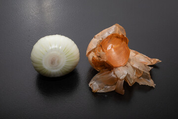 Peeled onion and onion peel next to it on black table and vegetable peeling knife.Close up of dry...