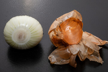 Peeled onion and onion peel next to it on black table and vegetable peeling knife.Close up of dry...