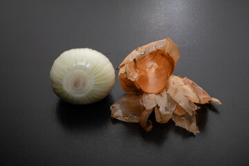 Peeled onion and onion peel next to it on black table and vegetable peeling knife.Close up of dry...