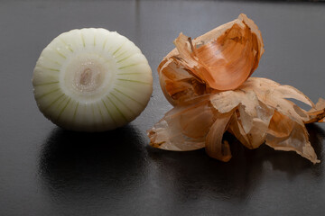 Peeled onion and onion peel next to it on black table and vegetable peeling knife.Close up of dry...