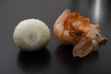 Peeled onion and onion peel next to it on black table and vegetable peeling knife.Close up of dry...